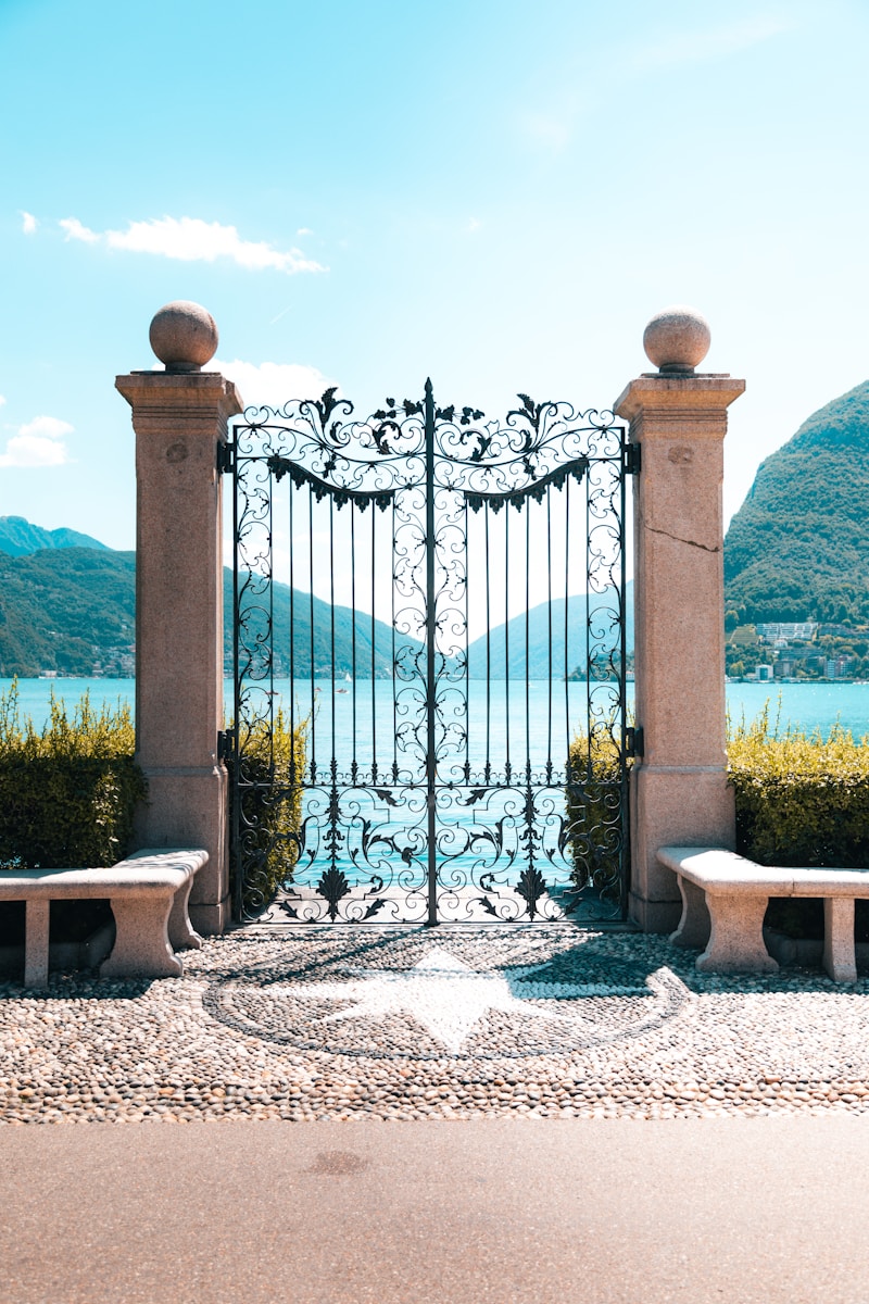 a gate with a stone fence and a body of water in the background